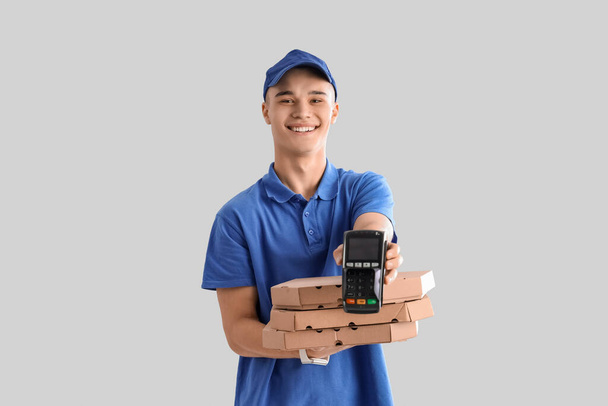 Young courier with pizza and payment terminal on light background - Photo, Image