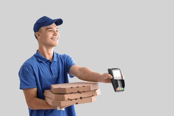 Young courier with pizza and payment terminal on light background - Photo, Image