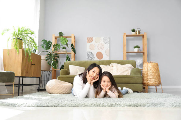 Азиатская мать со своей маленькой дочерью, лежащей на полу дома - Фото, изображение