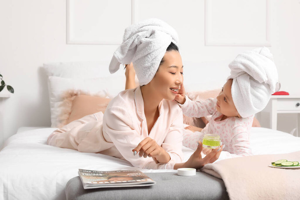 ベッドルームでフェイシャルクリームを塗る彼女の小さな娘とアジアの母親 - 写真・画像