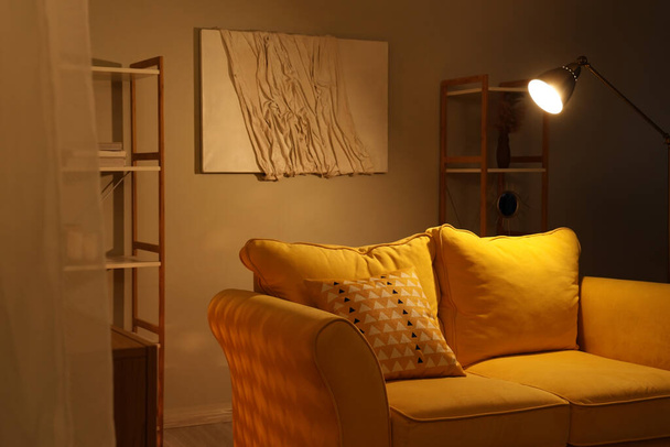 Innenraum des Wohnzimmers mit Sofa und glühender Lampe in der Nacht - Foto, Bild