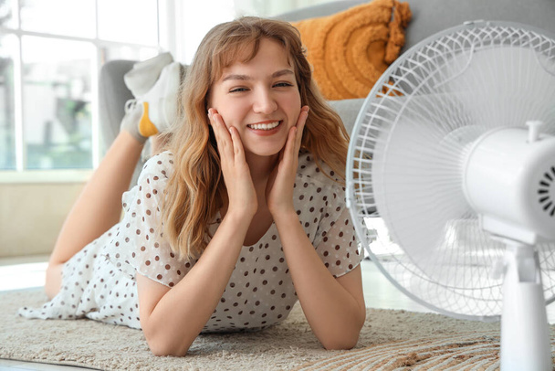 Bella giovane donna felice con ventilatore elettrico sdraiato sul pavimento in soggiorno - Foto, immagini