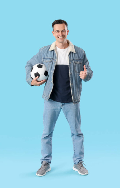 Молодой человек с футбольным мячом показывает большой палец вверх на синем фоне - Фото, изображение