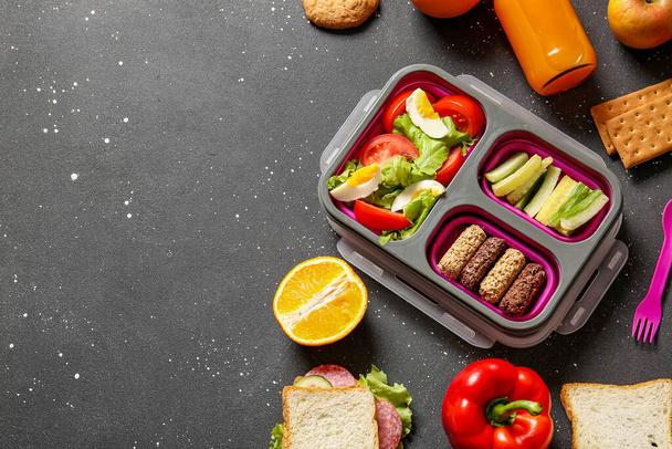 Lunchbox met heerlijk eten en een fles sap op grunge zwarte achtergrond - Foto, afbeelding