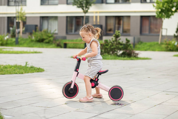 Pikkutyttö ajaa tasapainopyörällä ulkona. Opettelen ajamaan pyöräkonseptia. Kaupungit. - Valokuva, kuva