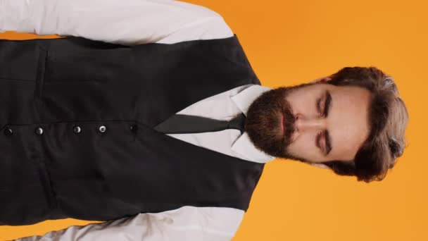 Vertical video Before serving meal, elegant waiter poses with reliability in front of a yellow background in studio. Bearded server in suit operating in formal environment in the culinary sector. - Footage, Video