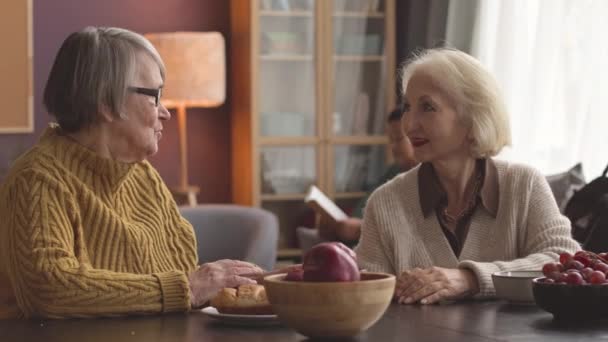Twee blanke oudere vrouwen hebben een gesprek aan tafel in een gezellig verpleeghuis - Video