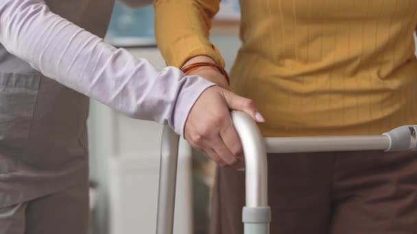 Tiro cortado de mulher idosa irreconhecível apoiando-se em caminhantes enquanto caminhava e enfermeira ajudá-la - Filmagem, Vídeo