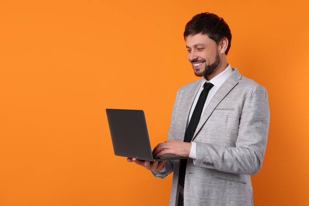 Happy man with laptop on orange background, space for text - Zdjęcie, obraz