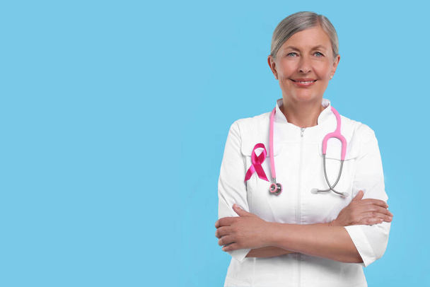 Doctor with pink ribbon and stethoscope on light blue background, space for text. Breast cancer awareness - Fotografie, Obrázek