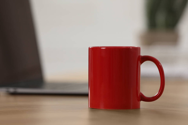 Red ceramic mug on wooden table at workplace. Space for text - Photo, Image