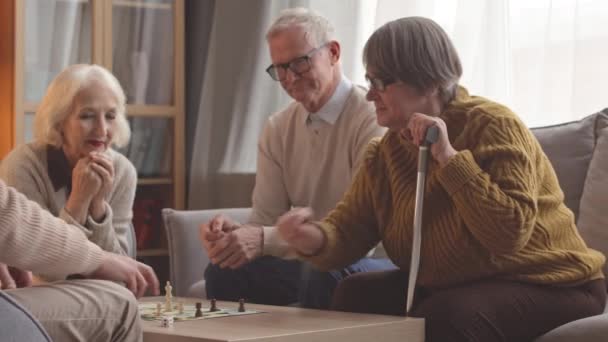 Allegro anziani lanciando dadi durante il gioco da tavolo a tavola in accogliente casa di cura - Filmati, video