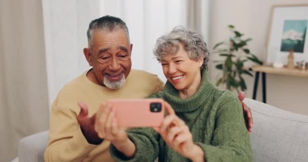 Starsza para, miłość i szczęśliwe selfie na domowej sofie dla mediów społecznościowych. Międzyrasowy mężczyzna i kobieta razem w salonie do zdjęcia profilowego, zaangażowania lub pamięci małżeństwa i szczęścia na emeryturze. - Materiał filmowy, wideo