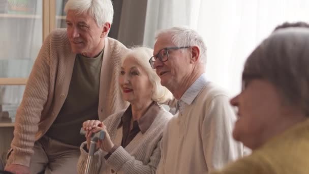 Négy fiatal kaukázusi nyugdíjas ül a kanapén az idősek otthonában, beszélgetnek, miközben együtt tévéznek. - Felvétel, videó