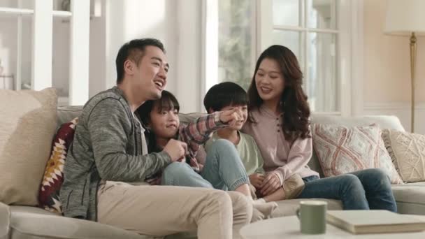 gelukkig aziatisch familie zitten op bank thuis kijken tv samen - Video