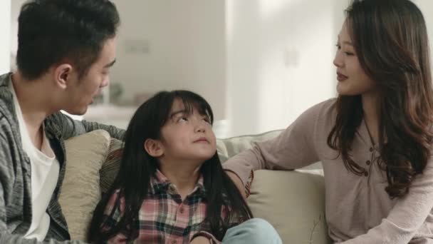 молодые азиатские родители сидят на семейном диване дома и приятно беседуют с дочерью - Кадры, видео