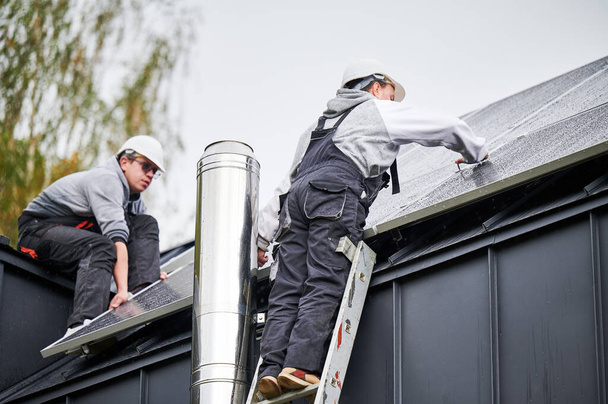 Instaladores instalando paneles solares fotovoltaicos en el techo de la casa. Los hombres ingenieros en cascos que construyen el sistema del módulo solar con la ayuda de la llave hexagonal. Concepto de energía alternativa y renovable. - Foto, imagen