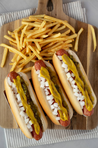 Hausgemachte frittierte Hot Dogs mit Senf, Zwiebeln und Essiggurke auf einem Holzbrett, von oben.  - Foto, Bild