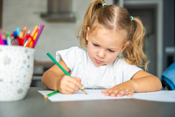 klein meisje tekent met gekleurde potloden in huis. Hoge kwaliteit foto - Foto, afbeelding