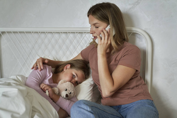 Madre llamando a un médico mientras su hija yacía enferma en la cama - Foto, imagen