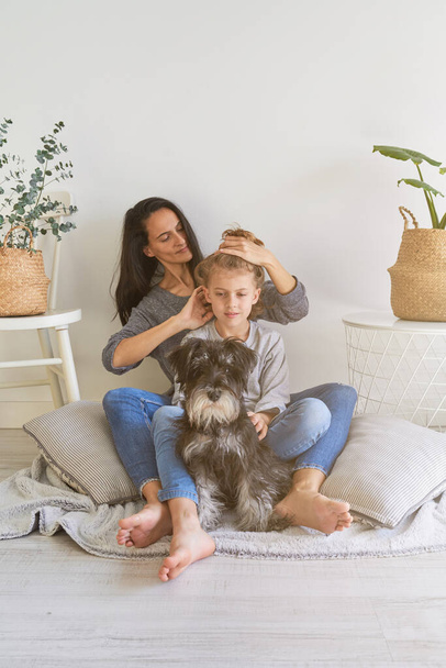 Friedliches Kind lockiges Haar und mit geschlossenen Augen zärtlich umarmt anonyme Mutter oben ohne, während sie in hellen Raum zu Hause sitzen  - Foto, Bild