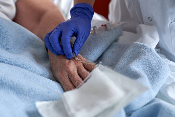 ラテックス手袋で匿名の医師をクロップ 病院で手術中に顔のない患者の手の静脈液のためにカテーテルを挿入する - 写真・画像