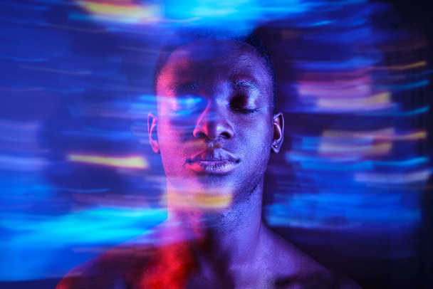 Άψυχος νεαρός Αφρο-Αμερικανός άνδρας με γυμνό κορμό στέκεται με τα μάτια κλειστά σε θολή μπλε φώτα στο σκοτεινό στούντιο - Φωτογραφία, εικόνα
