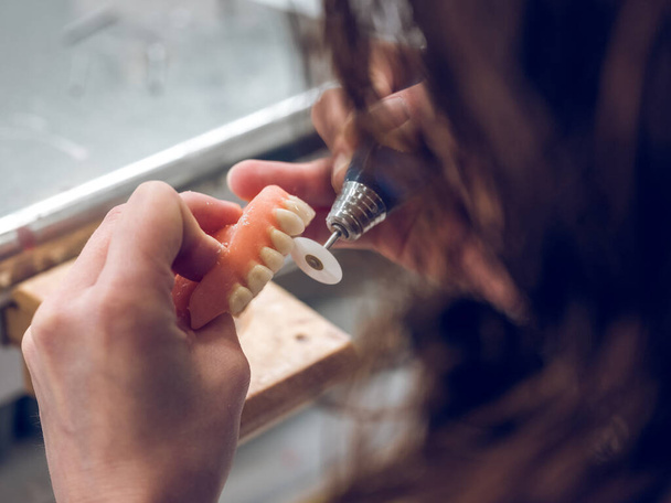 Сверху безликий анонимный зубной техник полирует протез с помощью роторной машины в селективном фокусе - Фото, изображение