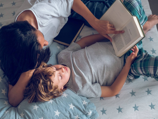 Top view of preteen boy and mom reading interesting book while lying on bed - Photo, Image