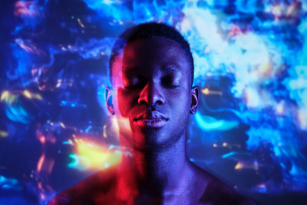 Doppelbelichtung ruhiger afroamerikanischer Mann mit nacktem Oberkörper, der mit geschlossenen Augen vor verschwommenem dunklen Hintergrund im Neonlicht steht - Foto, Bild