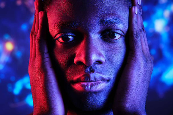 Грустный афроамериканец с руками на лице и красочными огнями, смотрящими в камеру - Фото, изображение