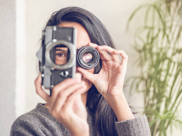 レトロなアナログ写真のカメラで穴を通して見ている長い暗い髪の認識できない女性と,レンズで目を覆い,写真を撮るふりをしながら - 写真・画像
