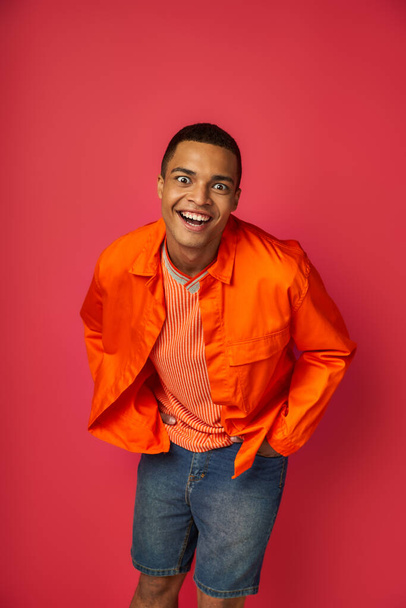 overjoyed and funny african american man, crazy face expression looking at camera on red background - Фото, зображення