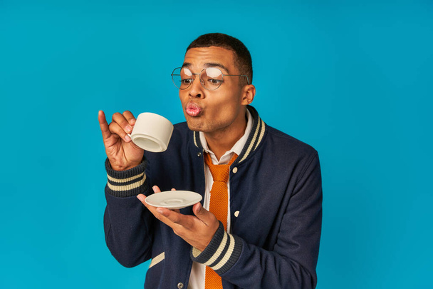 african american student in stylish jacket and eyeglasses holding coffee cup and saucer on blue - Photo, Image