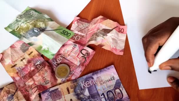 Begroting op papier schrijven. Bankbiljetten van Kenia op de achtergrond. Begrotingsconcept. - Video