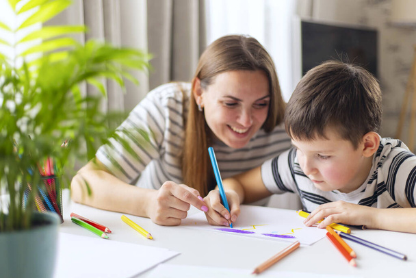 Счастливая семейная концепция. Мать и ее сын рисуют вместе. Взрослая женщина помогает парню рисовать.. - Фото, изображение