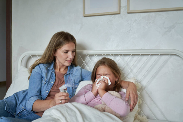 Ill elementary age girl blowing nose in bed at home - Photo, Image
