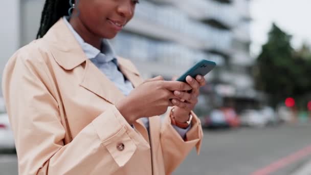 Επιχειρήσεις, μαύρη γυναίκα και smartphone στην πόλη για πληκτρολόγηση σε κοινωνικό δίκτυο, πληροφορίες ιστοσελίδας και επαφή στο διαδίκτυο. Ευτυχής εργαζόμενος ανάγνωση ειδήσεων app, μέσα ενημέρωσης ή κινητή επικοινωνία στο κινητό τηλέφωνο στην αστική οδό. - Πλάνα, βίντεο