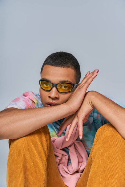 módní africký Američan v trendy slunečních brýlích a tie-dye tričku při pohledu na kameru na šedé - Fotografie, Obrázek