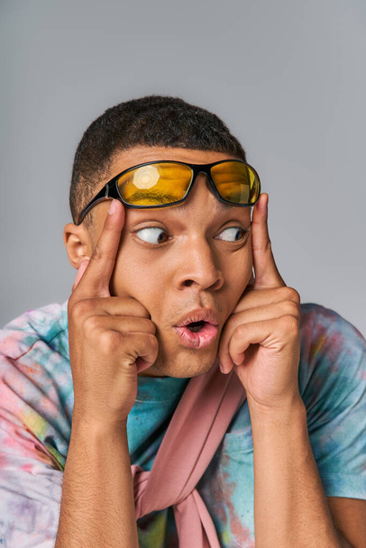 surprised african american man with stylish sunglasses looking away on grey - Fotó, kép