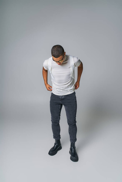 módní trend, africký Američan ve slunečních brýlích, tričko, džíny s rukama v kapsách na šedé - Fotografie, Obrázek