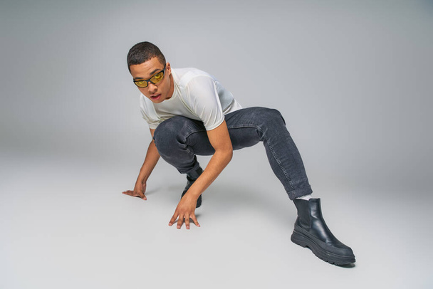 youth fashion, african american guy in t-shirt, jeans and sunglasses posing on grey - Foto, Imagem
