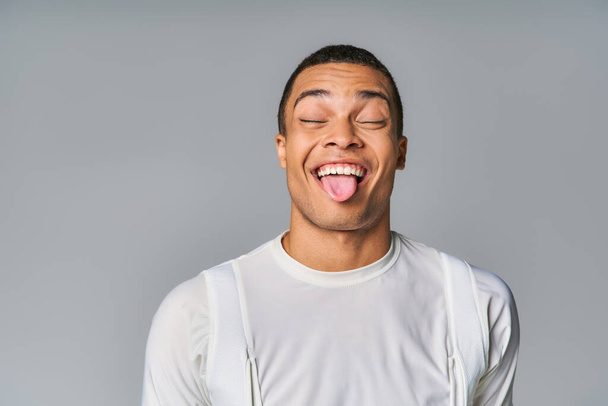 Komik Afro-Amerikan tişörtlü, kapalı gözlü, gri arka planda takılan - Fotoğraf, Görsel