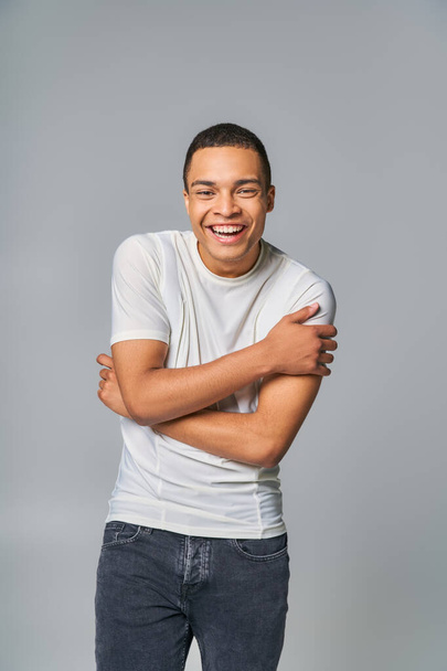 emocionado afroamericano en elegante camiseta mirando a la cámara y riendo en gris - Foto, Imagen