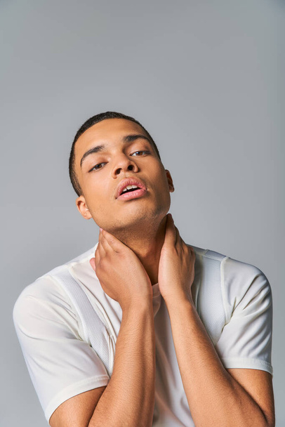 expressive and stylish african american man touching neck while posing on grey - Foto, Imagen