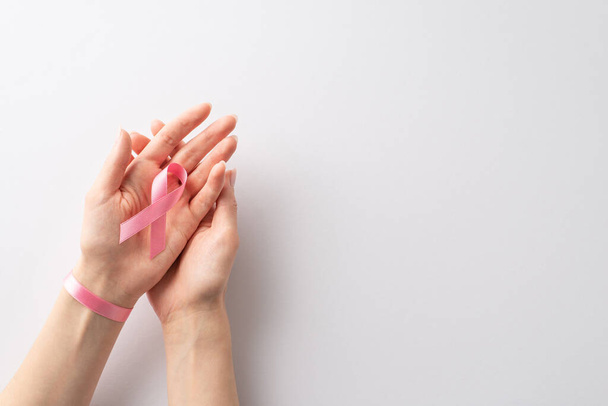 Mois de la sensibilisation au cancer du sein. D'en haut, des mains féminines bercent un ruban rose pastel sur un fond blanc isolé. Polyvalent pour le contenu promotionnel ou les messages texte - Photo, image