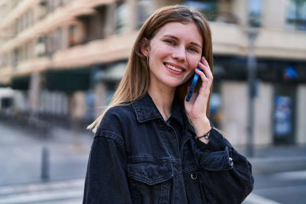 Młoda blondynka uśmiecha się pewnie rozmawiając przez smartfona na ulicy - Zdjęcie, obraz