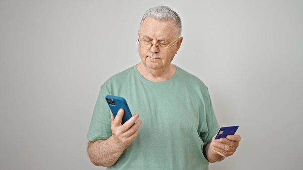 Седовласый мужчина средних лет делает покупки со смартфоном и кредитной картой на изолированном белом фоне - Фото, изображение