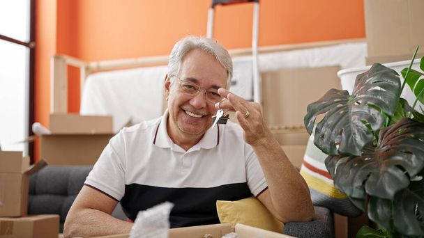 Mann mittleren Alters mit grauen Haaren lächelt zuversichtlich und hält neue Hausschlüssel in der neuen Wohnung - Foto, Bild