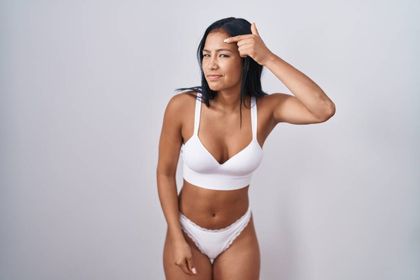 Latijns-Amerikaanse vrouw draagt lingerie die ongelukkig wijst naar puistjes op het voorhoofd, lelijke infectie van blackhead. acne en huidprobleem  - Foto, afbeelding